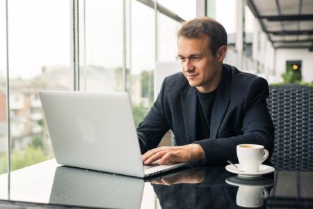 mężczyzna siedzący przy laptopie z kawą