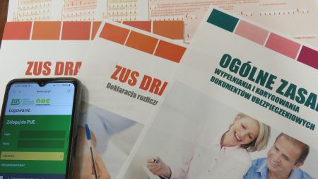 Zdjęcie z deklaracjami rozliczeń oraz smartfon z widoczną na wyświetlaczu stroną ZUS